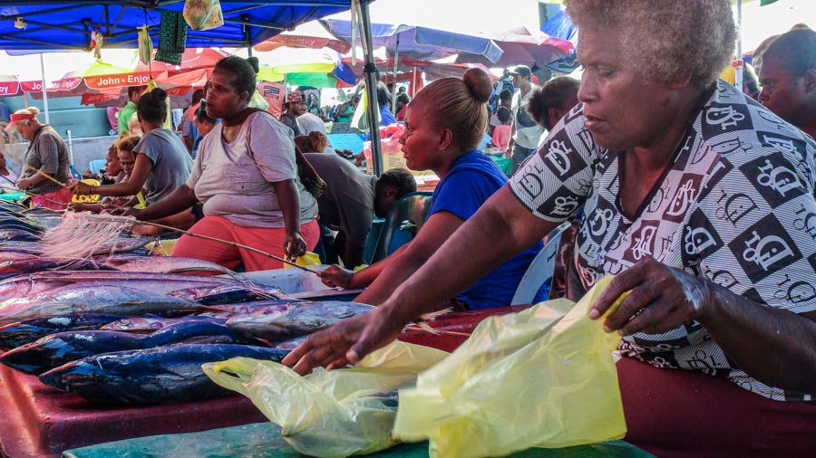 Women under awnings with tables laid with fresh tuna for sale at market