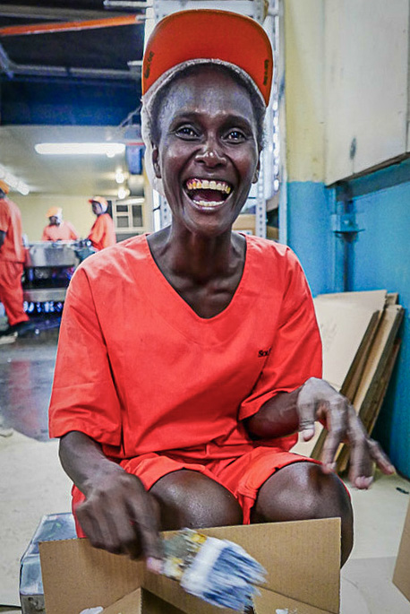 Laughing woman in orange cap and coverall clothing with paintbrush and box in factory Solomon Islands. Photo Francisco Blaha.