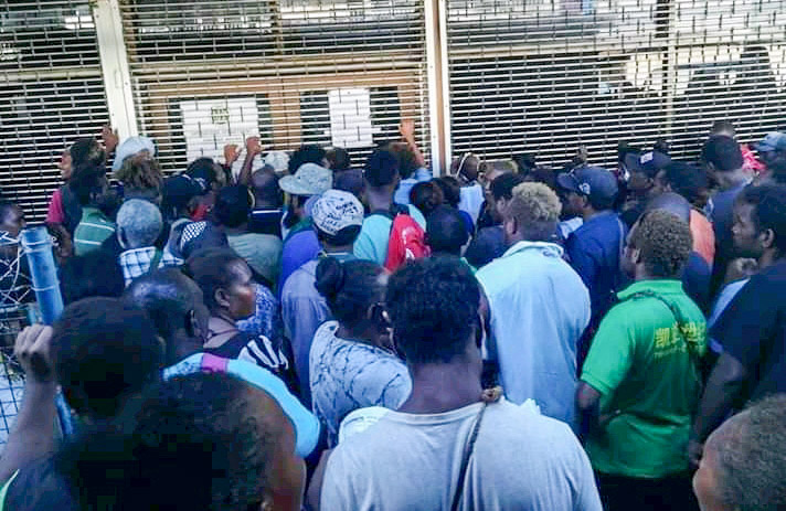 Densely packed group of Solomon Islanders outside building with security shutters down. Photo: Lachlan S. Eddie.