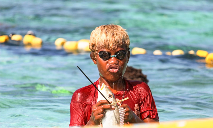Boy wearing swimming goggles stands was it deep in water holding a fish he has caught in Malaita managed marine areas. Photo:WorldFish/Bira'au Wilson Saeni.