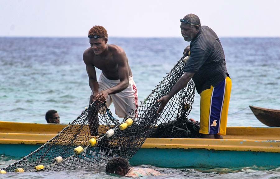 Two Fumamato'o men standing in open long boat haul in a net while fishing in the open-and-close area. Photo: WorldFish/Bira'au Wilson Saeni.