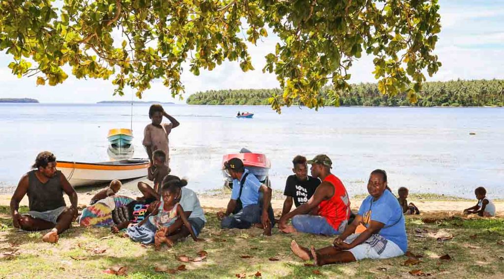 Group of women, men and children sitting under shade of tree on beach at Louna, Solomon Islands. Photo: Solomon Islands Government Communications Unit.