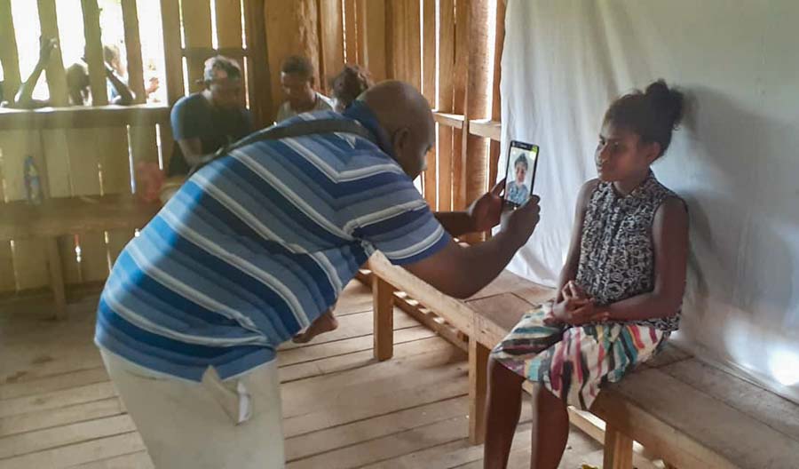 Man uses a tablet to take a photo of a young woman who is a tribal landowner at Bina Harbour, Malaita, Solomon Islands