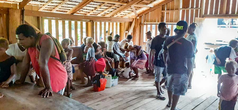 Bina Harbour women, men and children wait inside open-walled room to have names recorded as beneficiaries, Solomon Islands