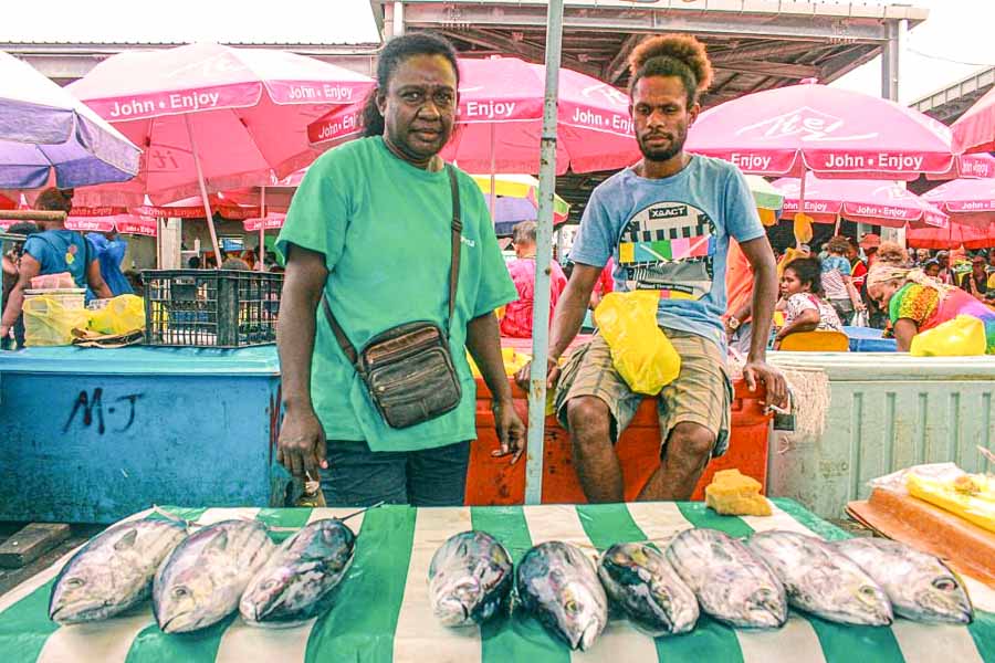 Sheroll Galo and John Kennedy were longtime salt fish vendors in Honiara. They are at a market, and positioned behind a table with 9 fish laid out on it, and in front of chiller boxes. Photo: George Maelagi.