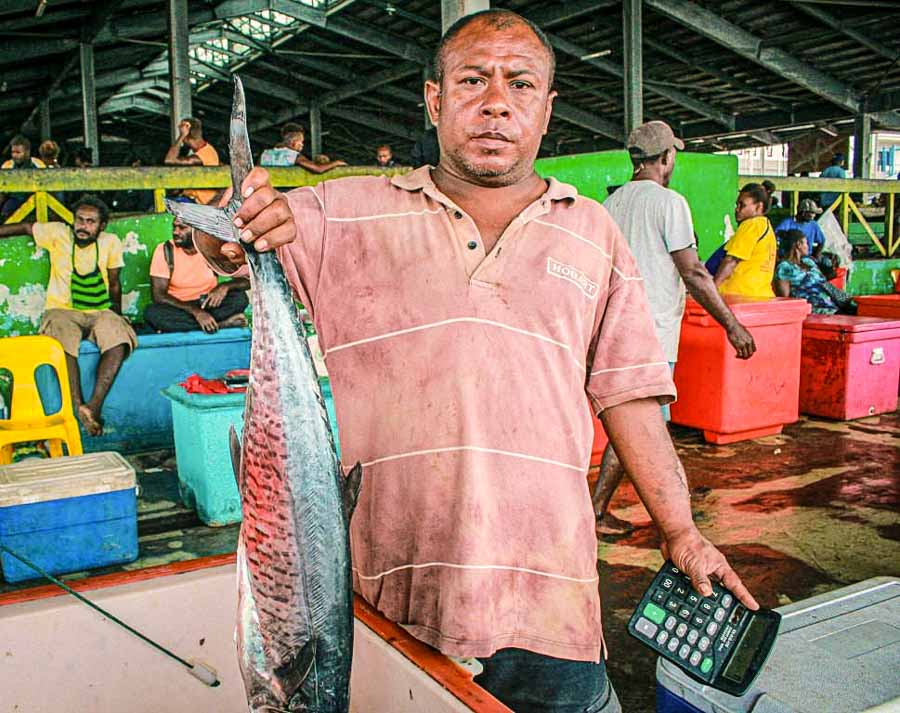 Sam, as he would want to be called, said the COVID-19 pandemic had had a huge impact on his fish-vending business at the Honiara Central Market. He stands at a market with a calculator in his left hand and a fish in his right. Photo: George Maelagi.