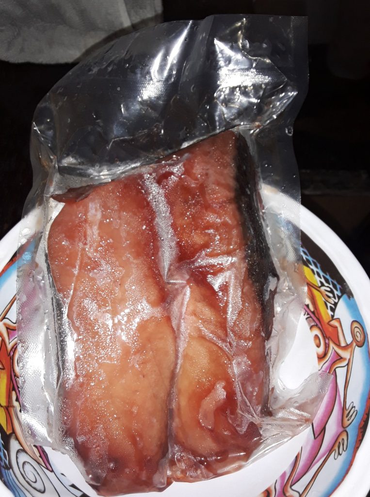 A vacuum sealed piece of fish fillet, pink with its skin on, in a colourful bowl