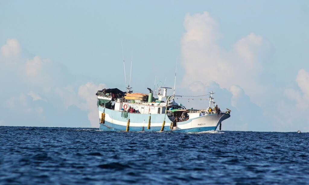 A blue and white fishing boat moves along the sea with fishing nets hanging over the sides