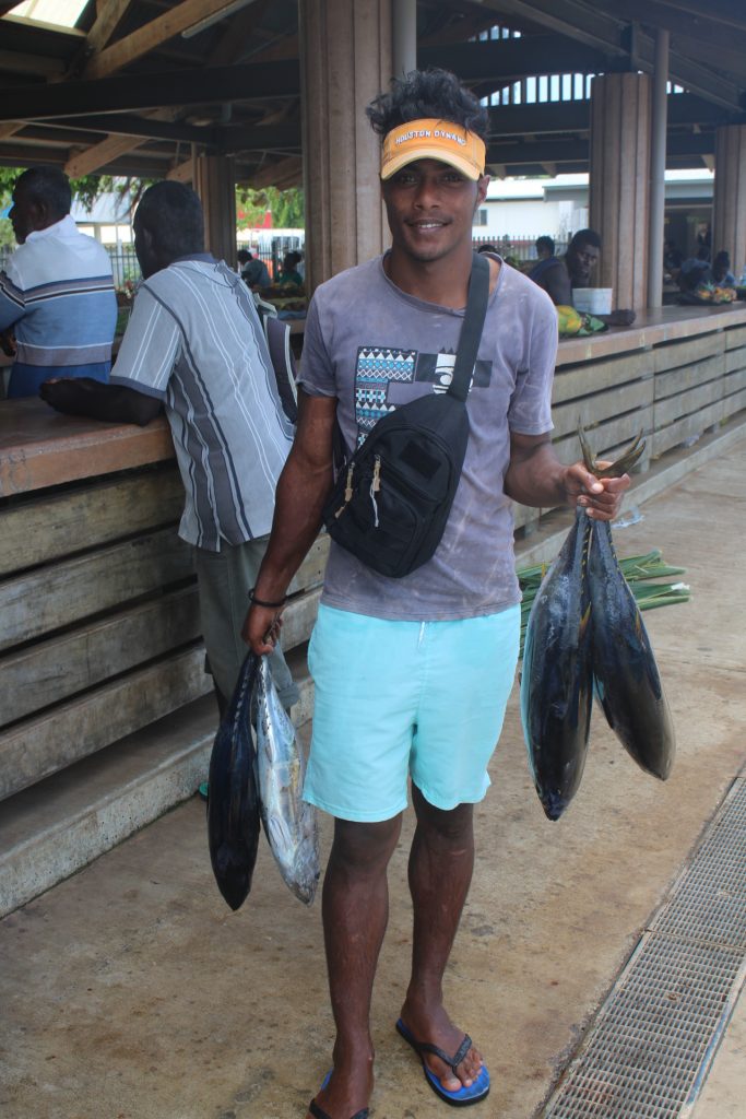 Young man holding 4 tuna standing near a market