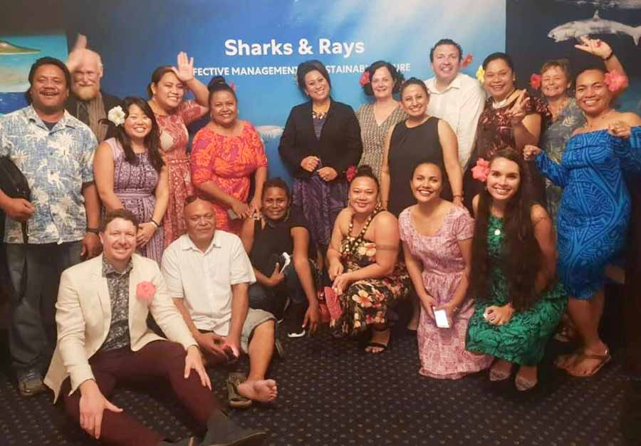 Group of 18 women and men, including some from Pacific Islands, standing before a shark poster