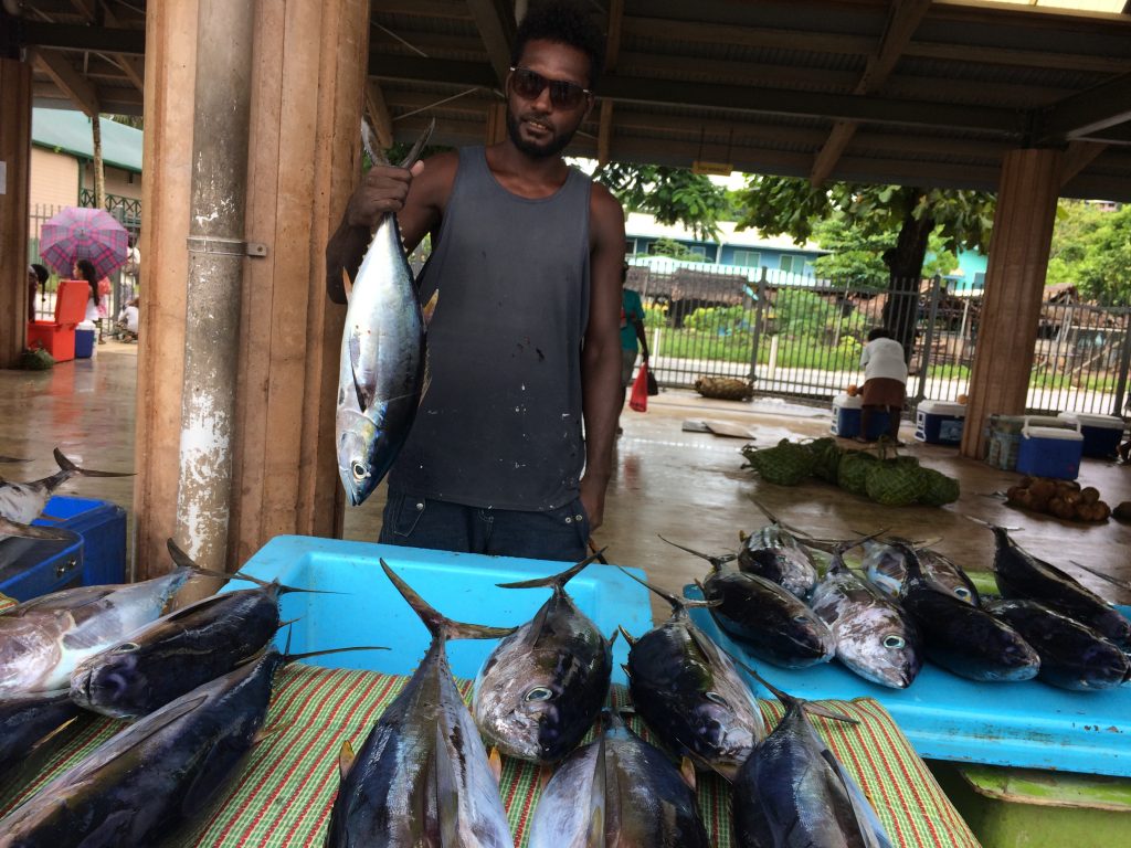 Man holding up a tuna for sale at a market near other tuna laid out